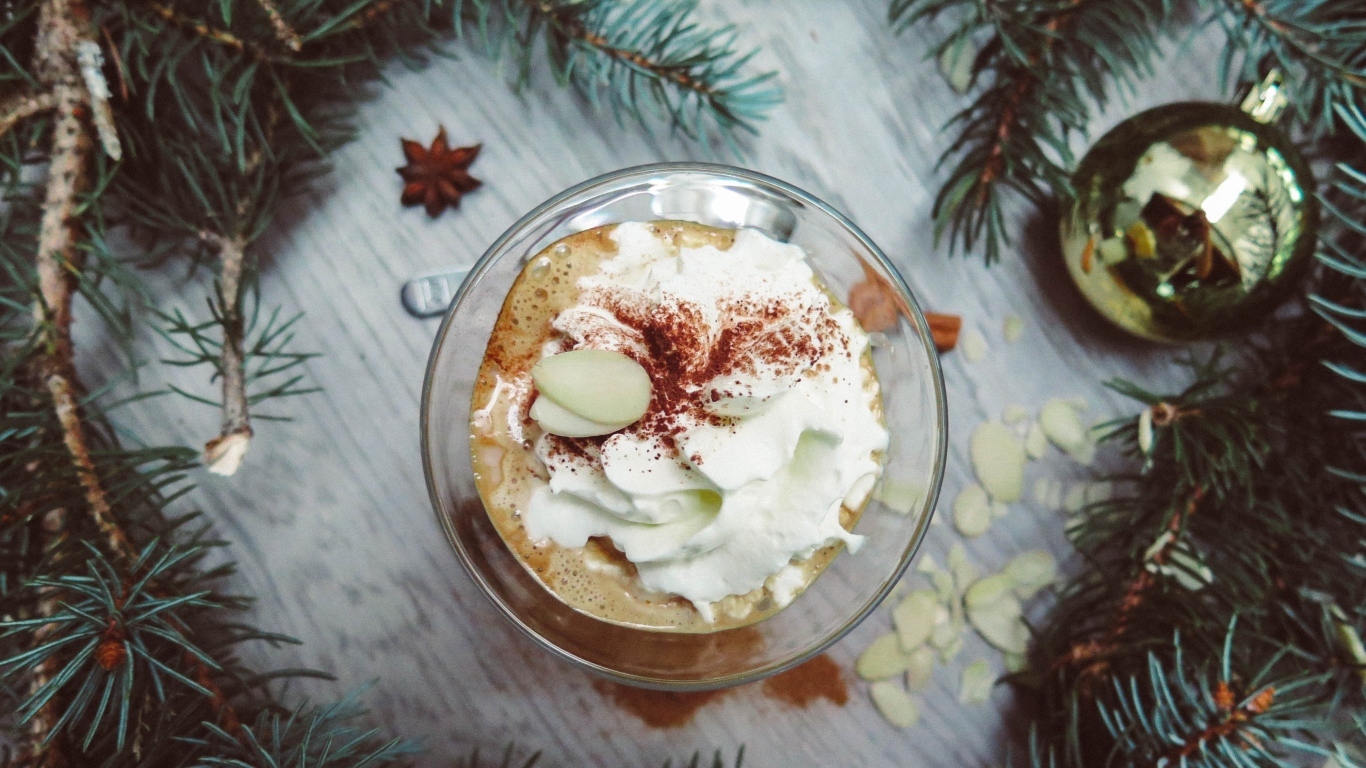 Горячий кофе с взбитыми сливками в чашке на столе с еловыми ветками