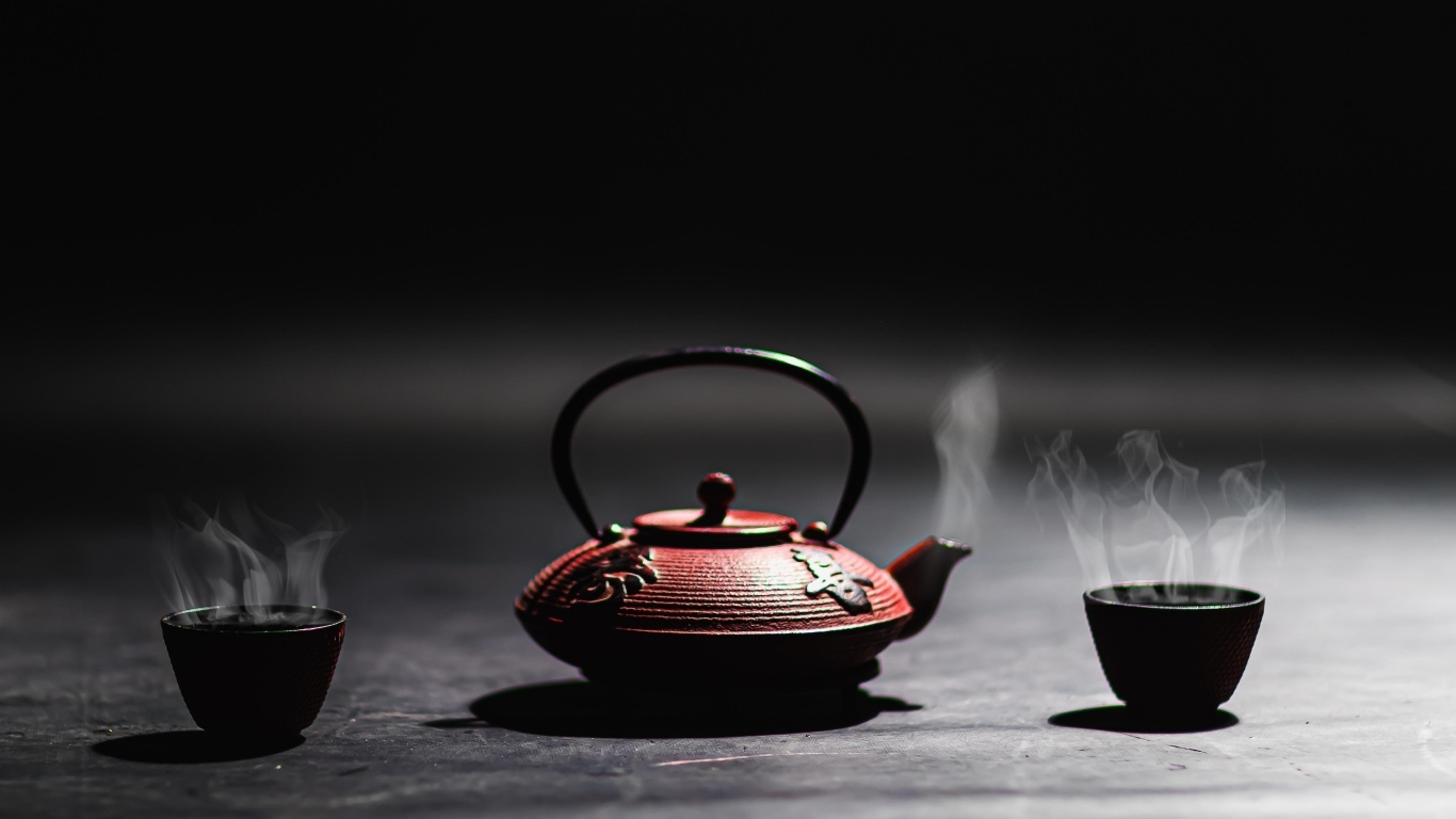 Чайник с горячим чаем на черном фоне