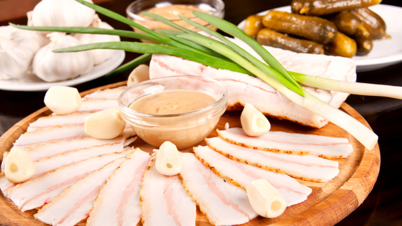 Нарезанное сало с чесноком и солеными огурцами на столе