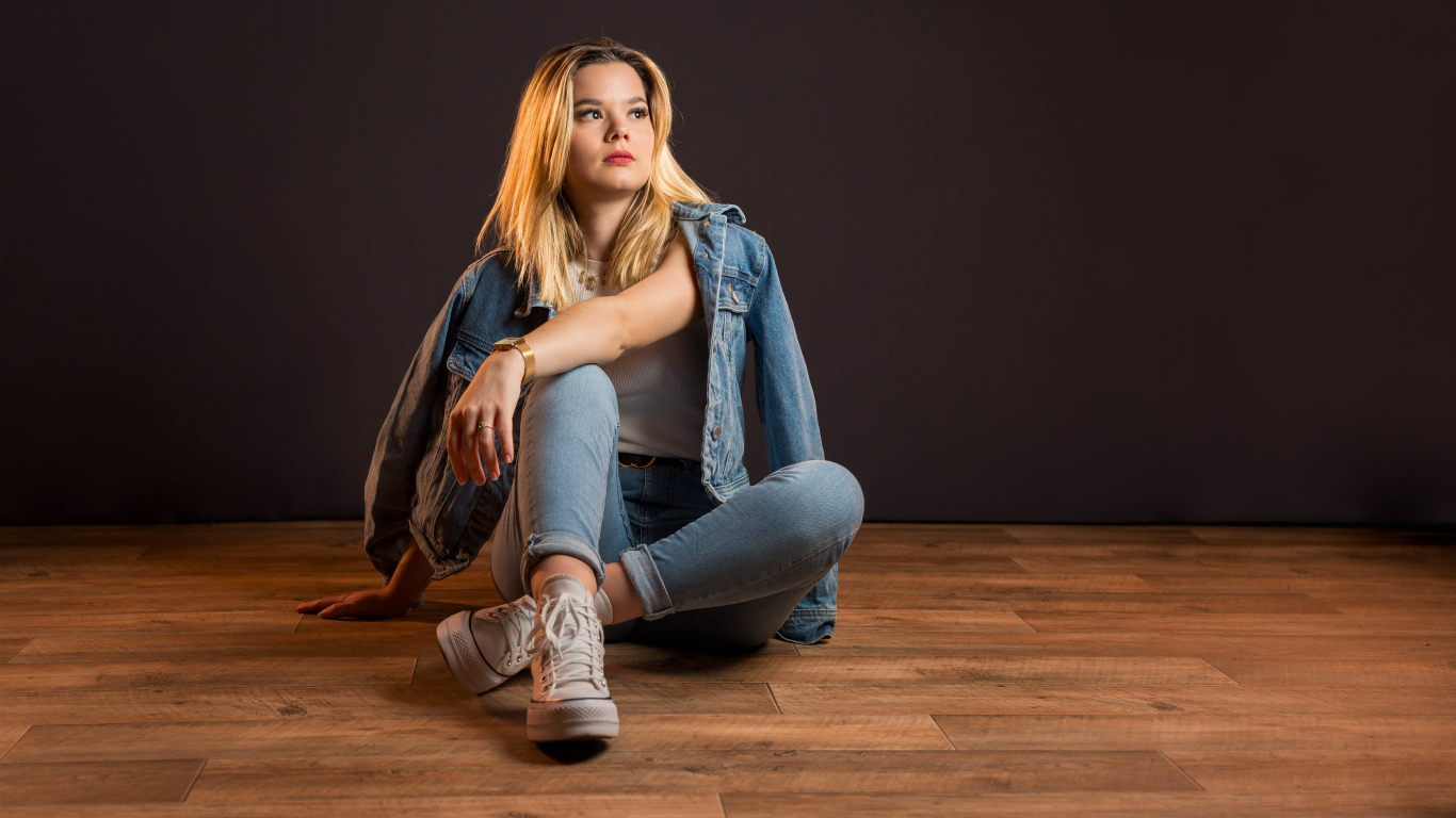 Девушка в джинсовом костюме сидит на полу