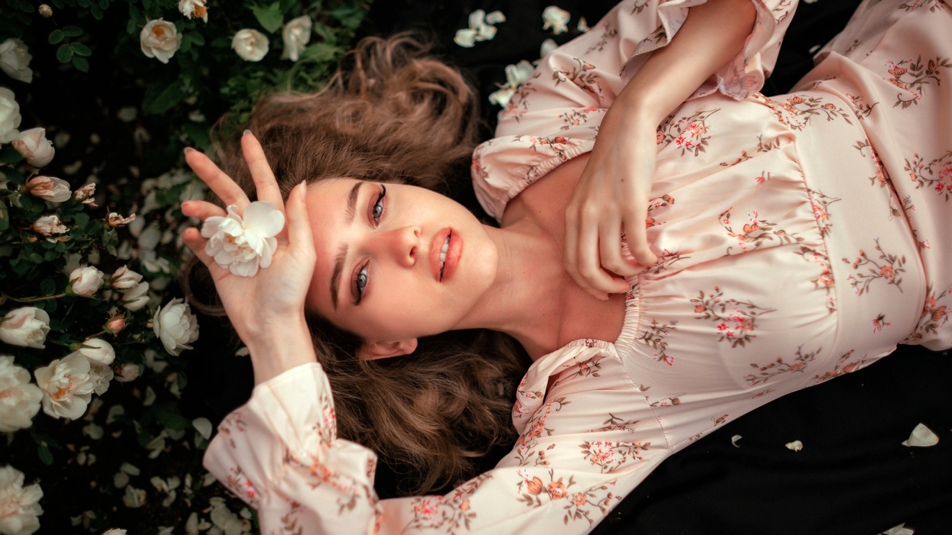 Девушка в розовом платье лежит на земле с цветами розы
