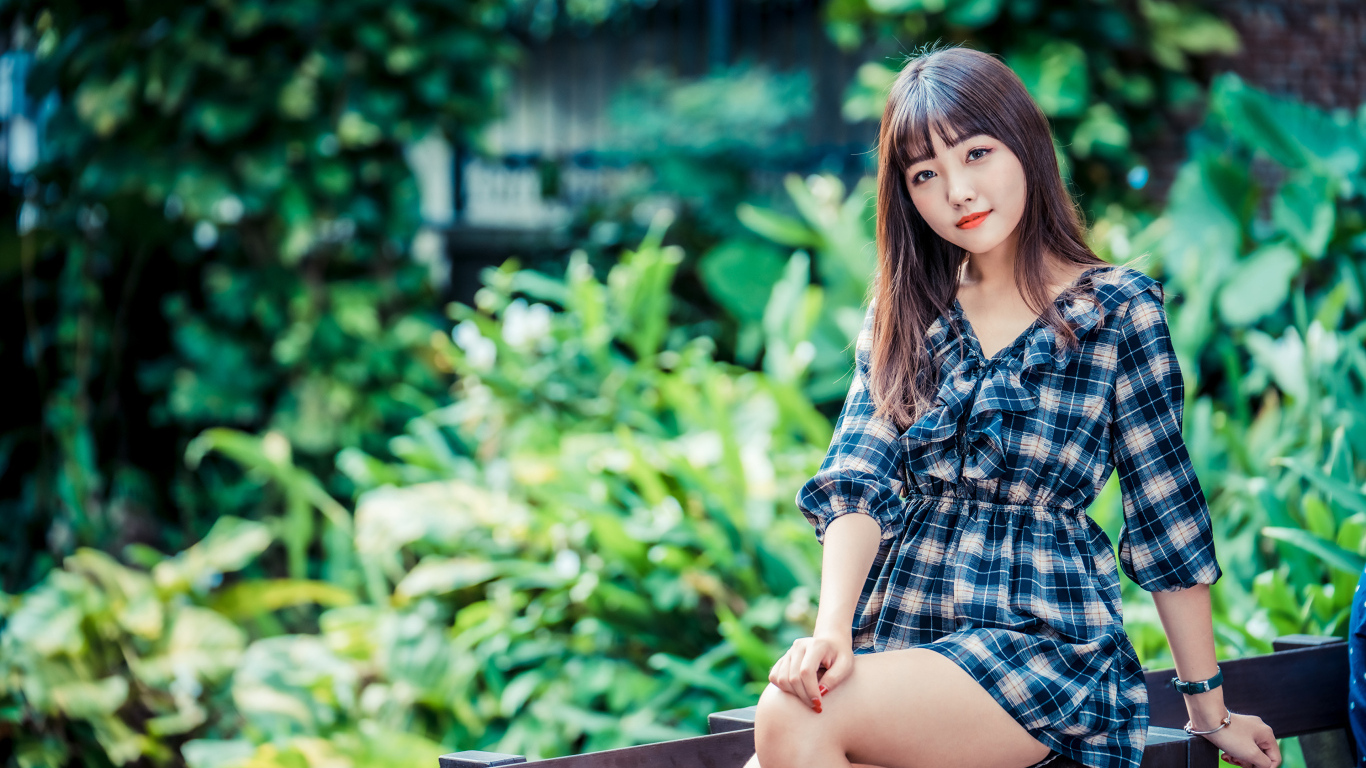 Молодая девушка в клетчатом платье сидит на заборе