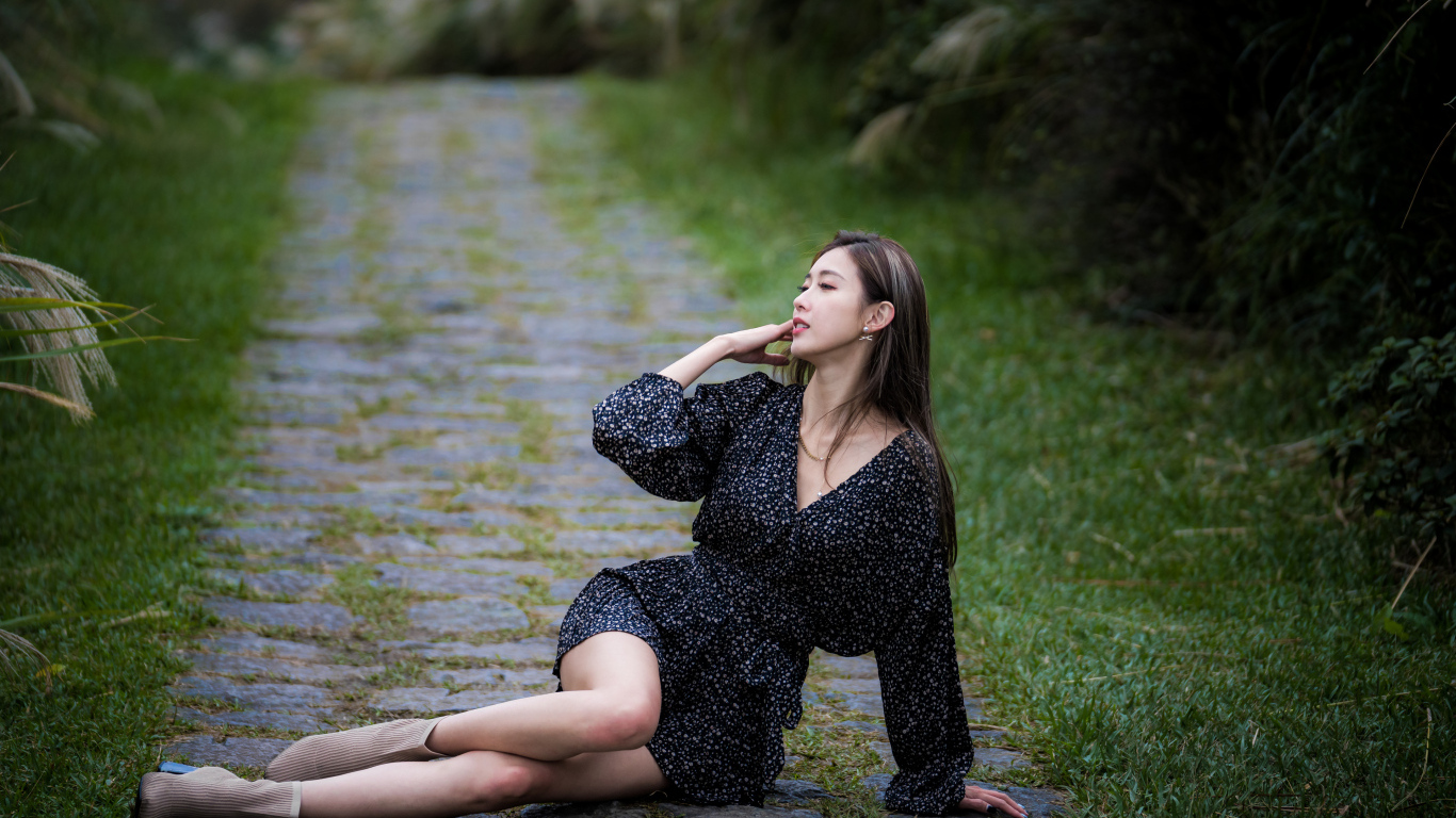 Девушка азиатка в платье лежит на дороге в парке