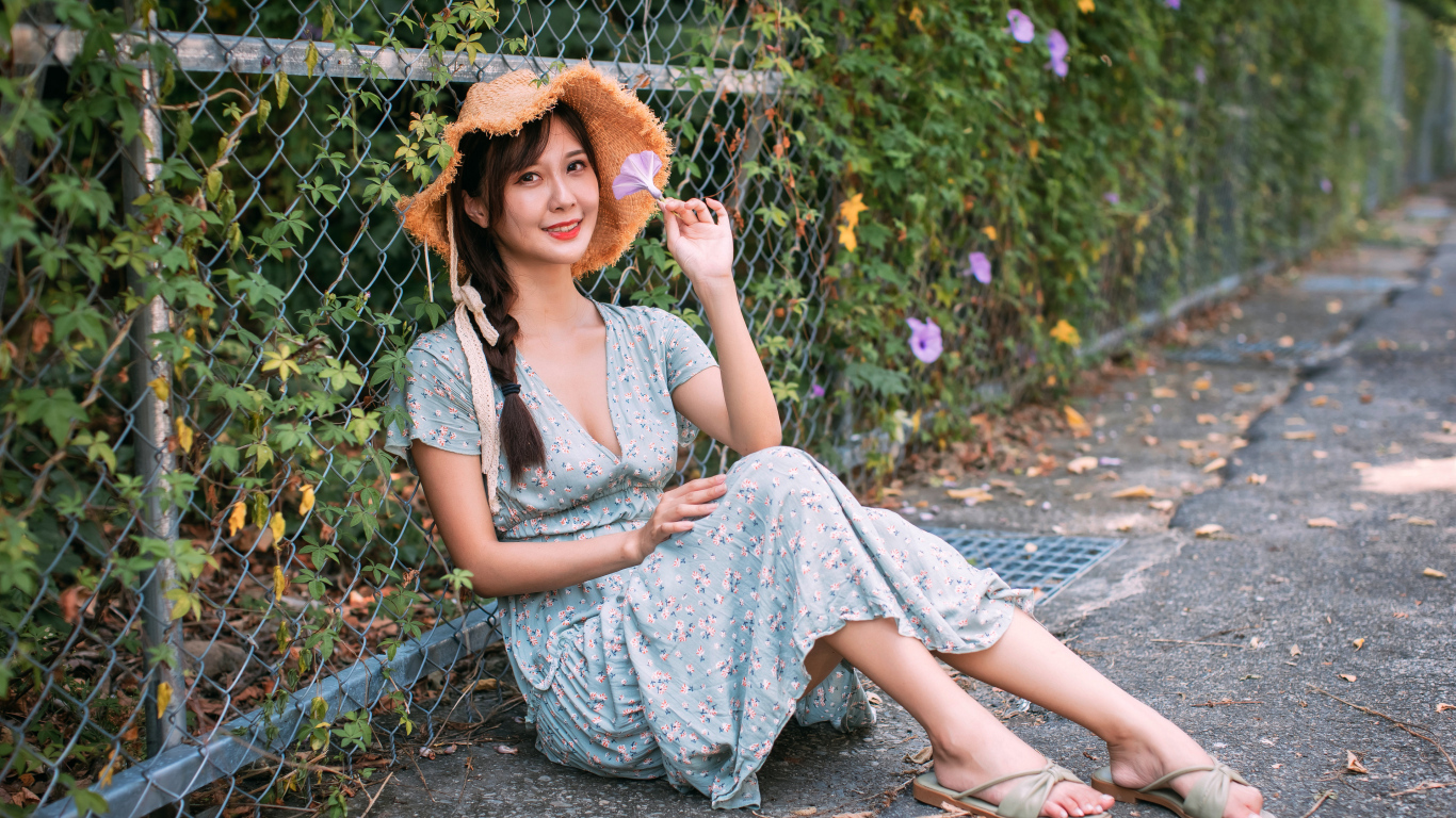 Девушка азиатка в платье сидит у забора