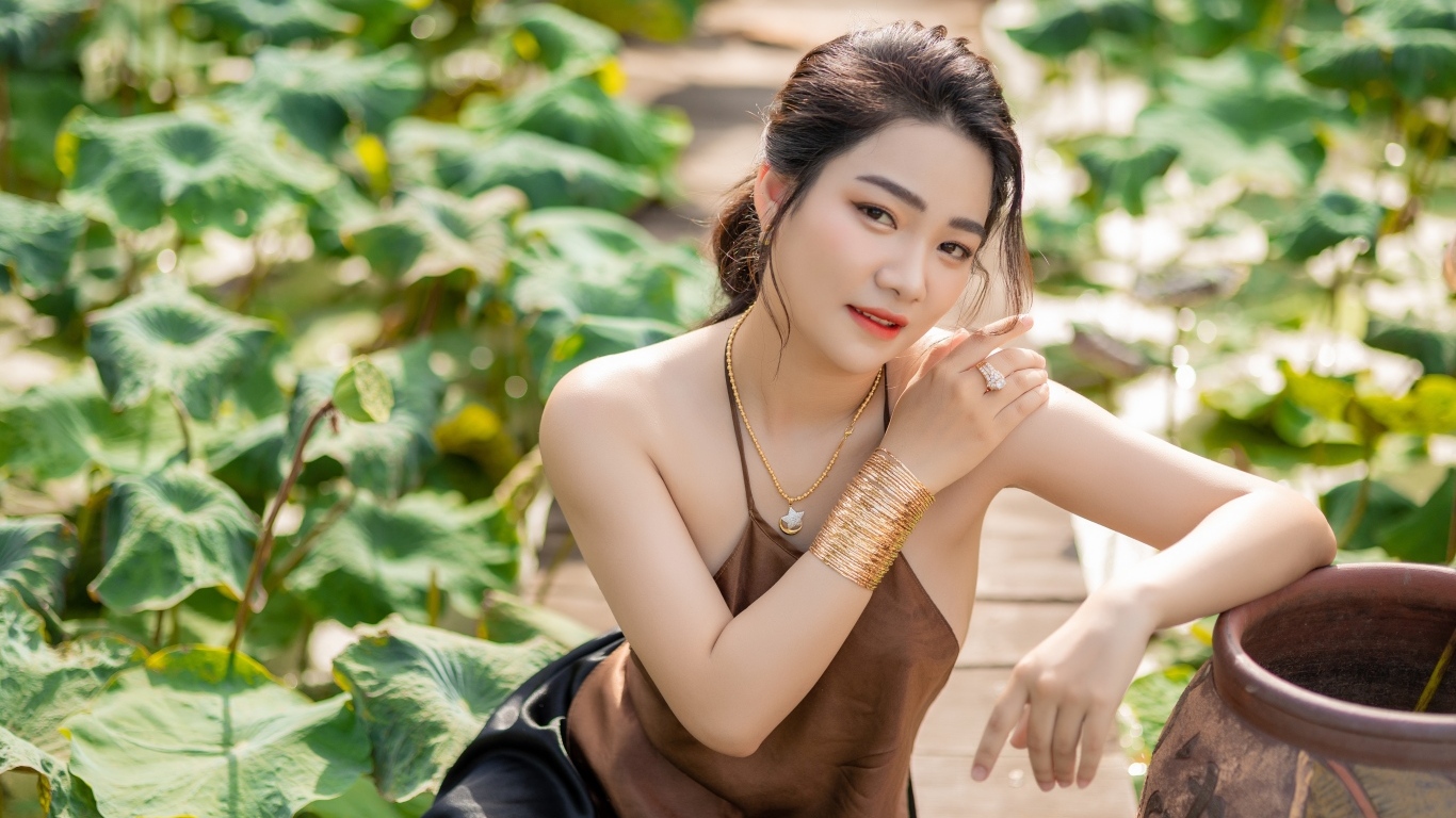 Девушка азиатка сидит у зеленых листьев лотоса