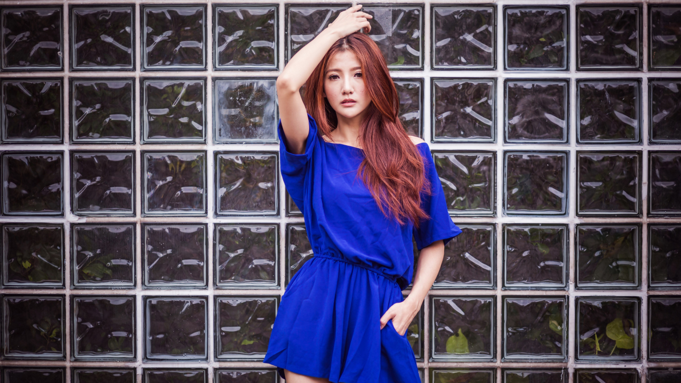 Азиатка в синем платье стоит у стеклянной стены