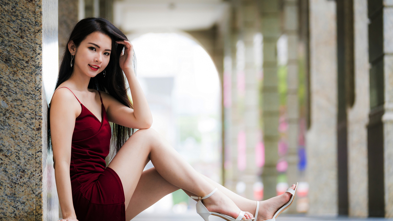 Азиатка в красном платье сидит у стены 