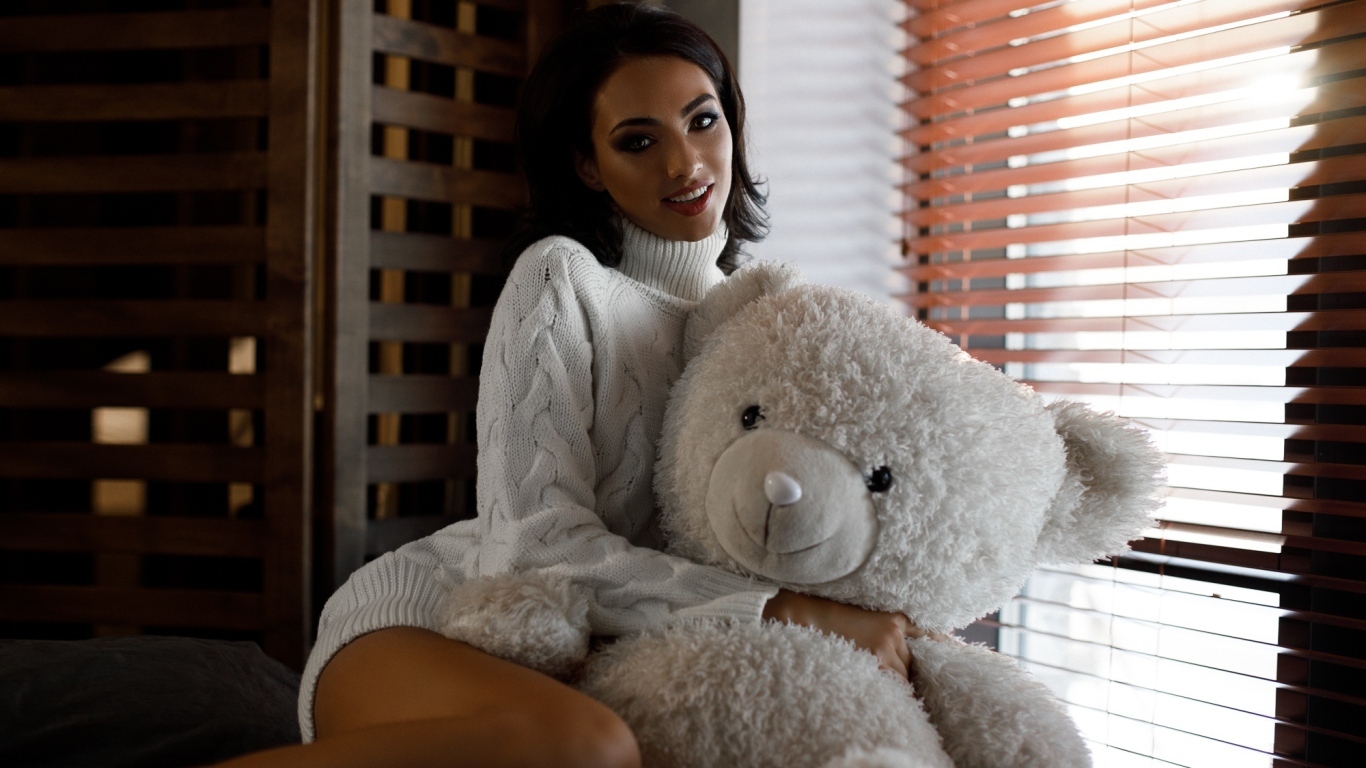 Красивая девушка в свитере с медведем у окна