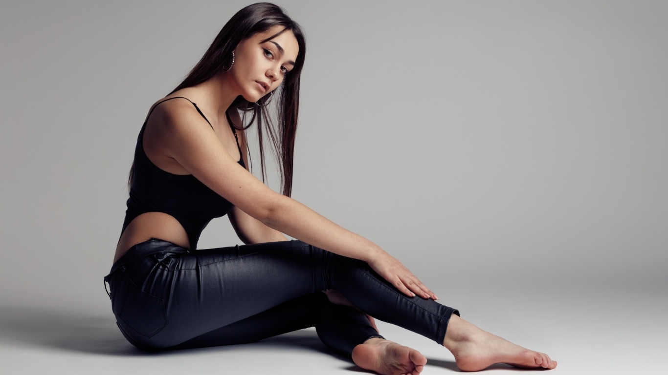 Красивая девушка в черных брюках на сером фоне