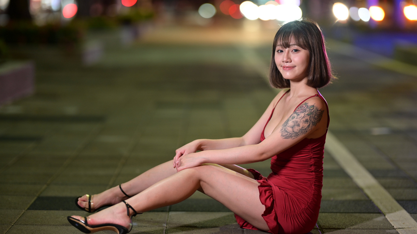 Милая азиатка в красном платье сидит на дороге