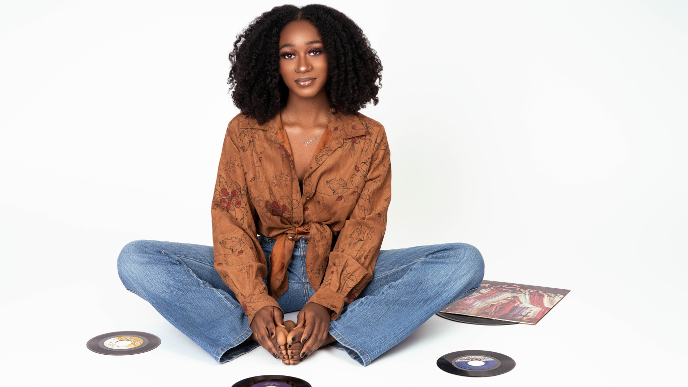 Темнокожая девушка сидит на белом фоне с пластинками