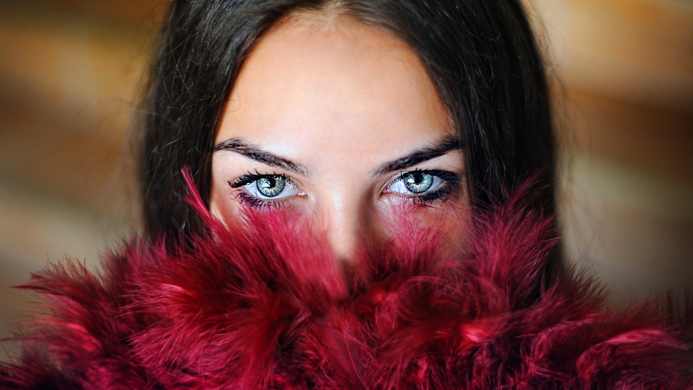 Девушка с красивыми глазами закрыла лицо красными перьями