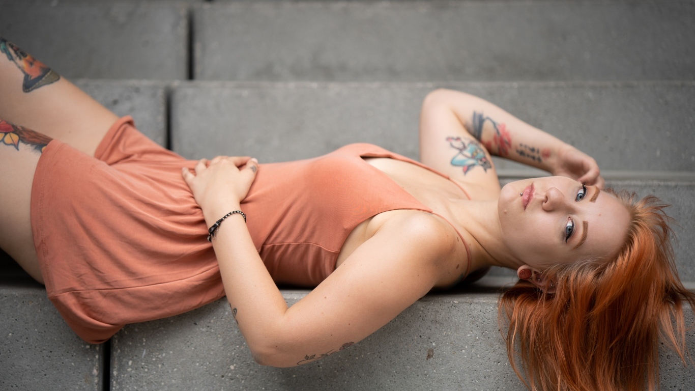 Рыжеволосая девушка с татуировками лижет на ступеньках