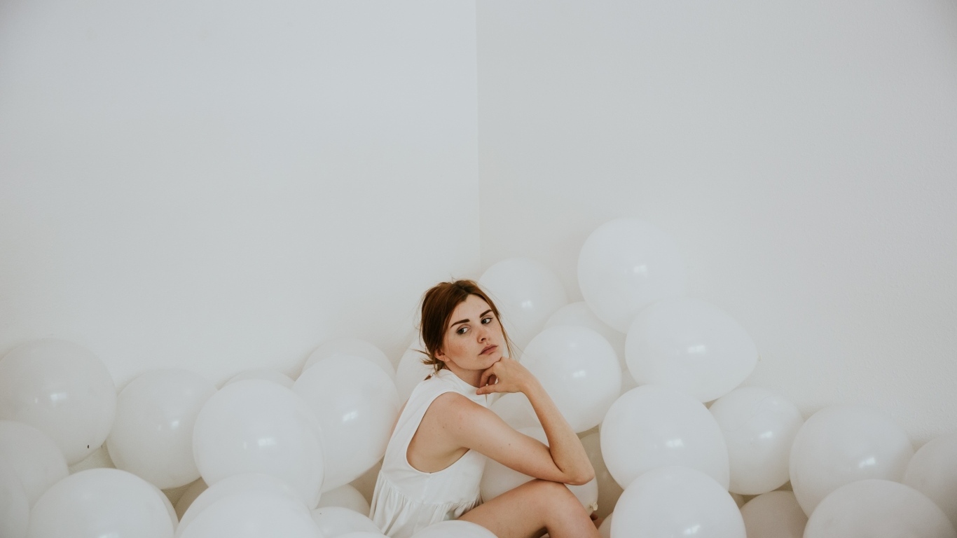 Грустная девушка сидит в белых воздушных шариках