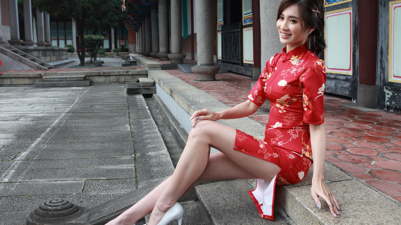 Улыбающаяся девушка азиатка в красном платье сидит на ступеньках