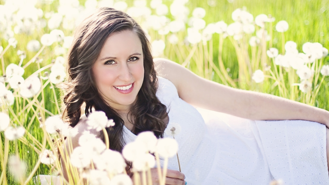 Улыбающаяся девушка лежит на поле с одуванчиками