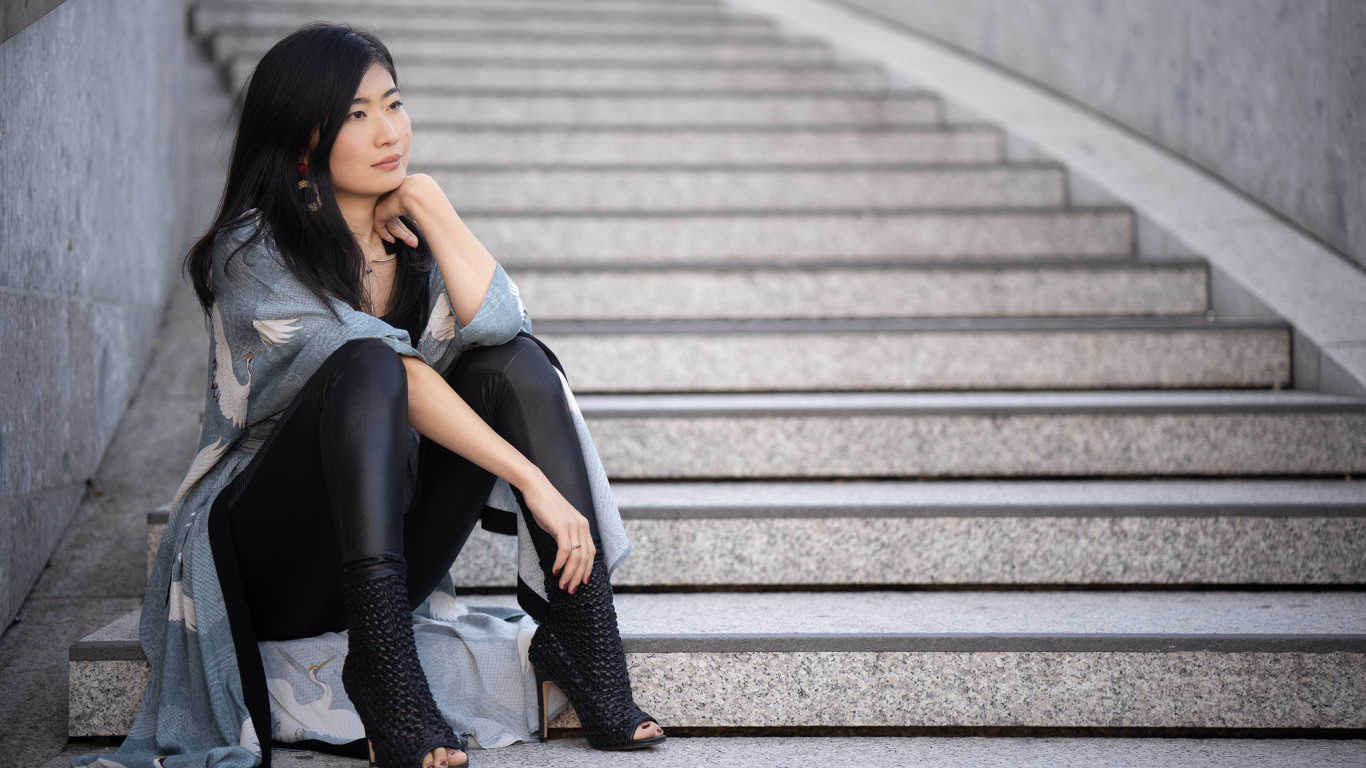 Задумчивая девушка азиатка сидит на ступеньках