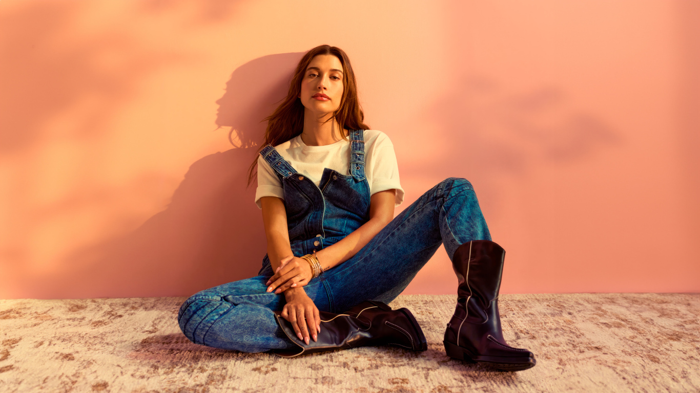 Американская модель Хейли Болдуин в джинсовом комбинезоне сидит у стены