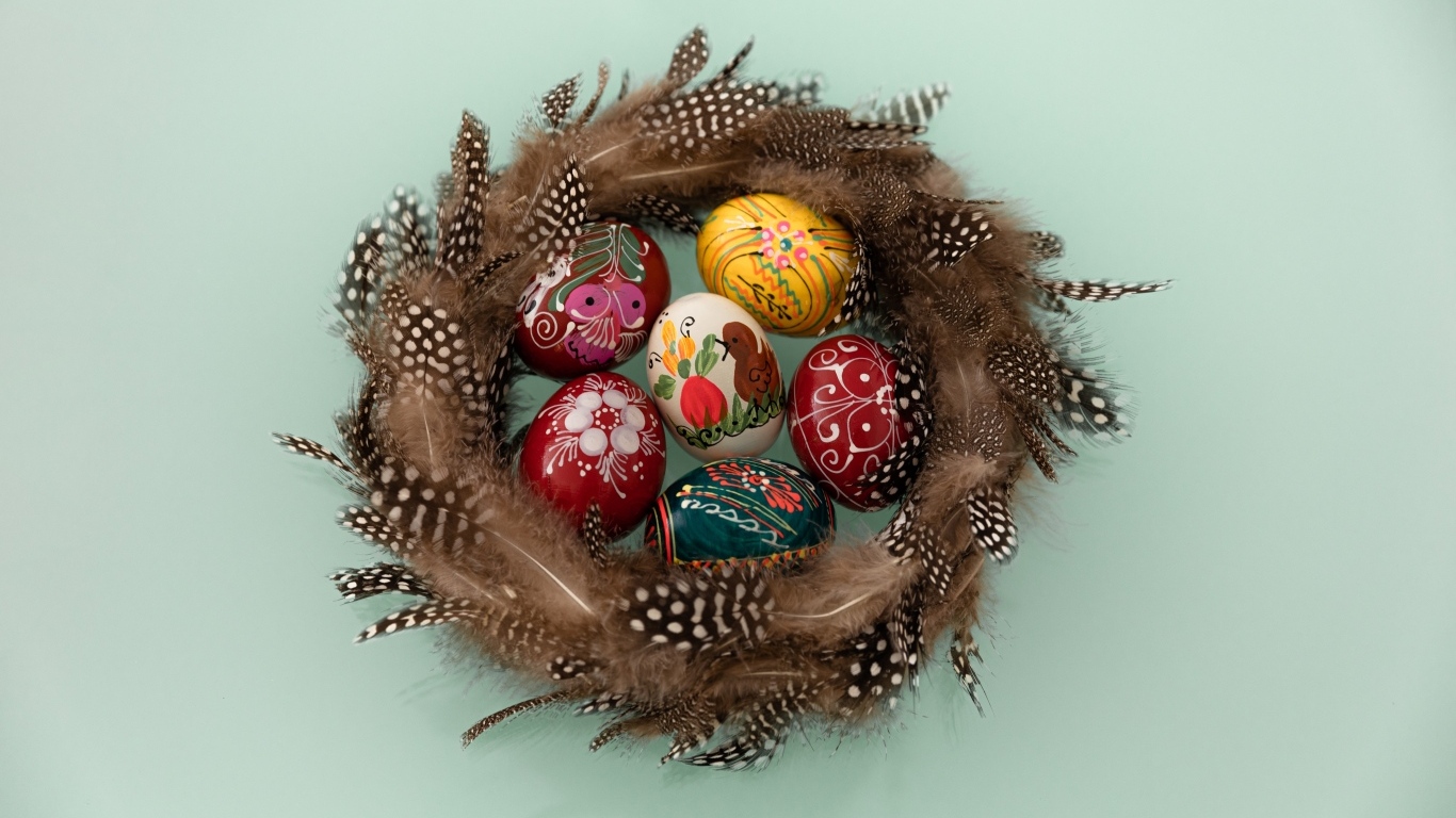 Красивые разноцветные яйца в гнезде из перьев на сером фоне