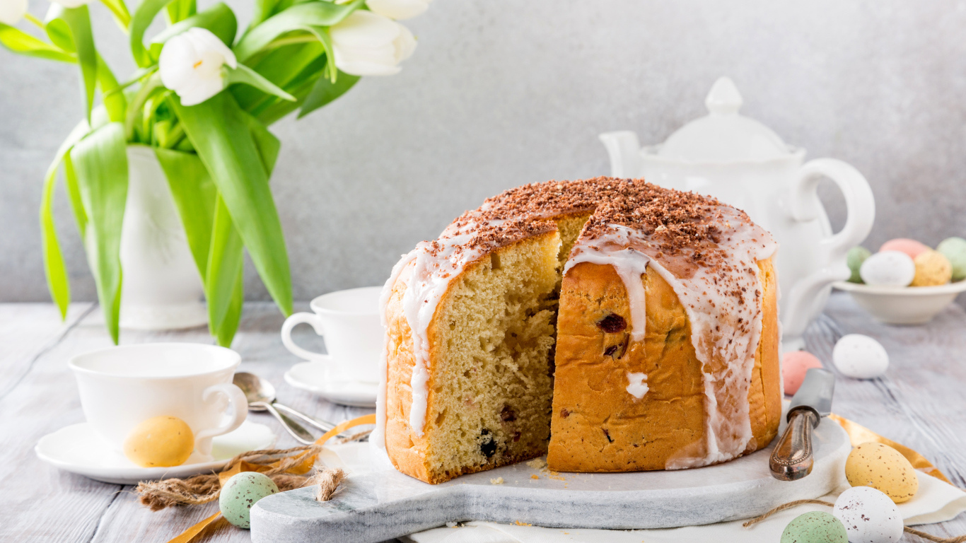 Пасхальный кулич на столе с букетом тюльпанов и сладостями