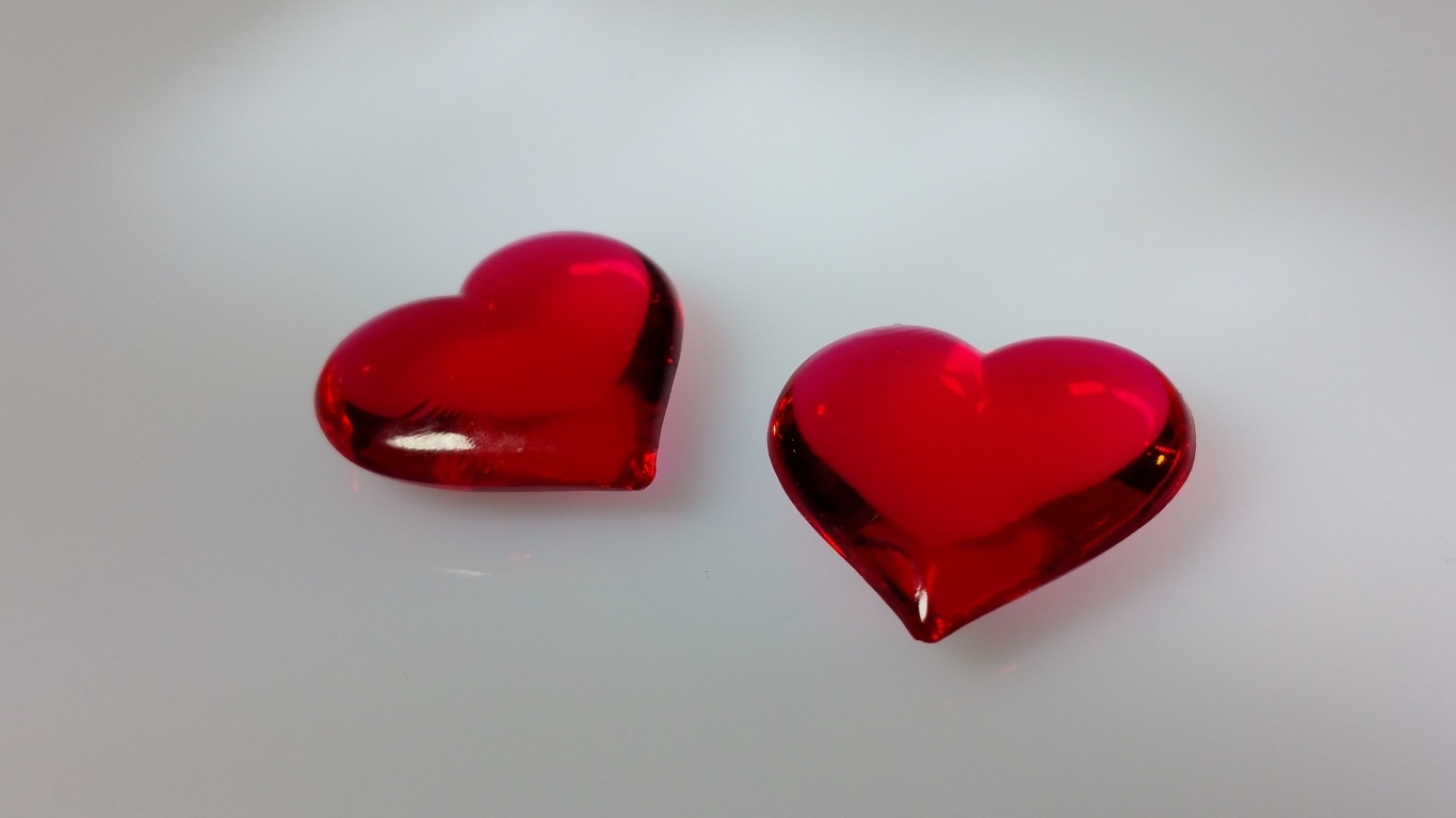 Два красных стеклянных сердца на сером фоне