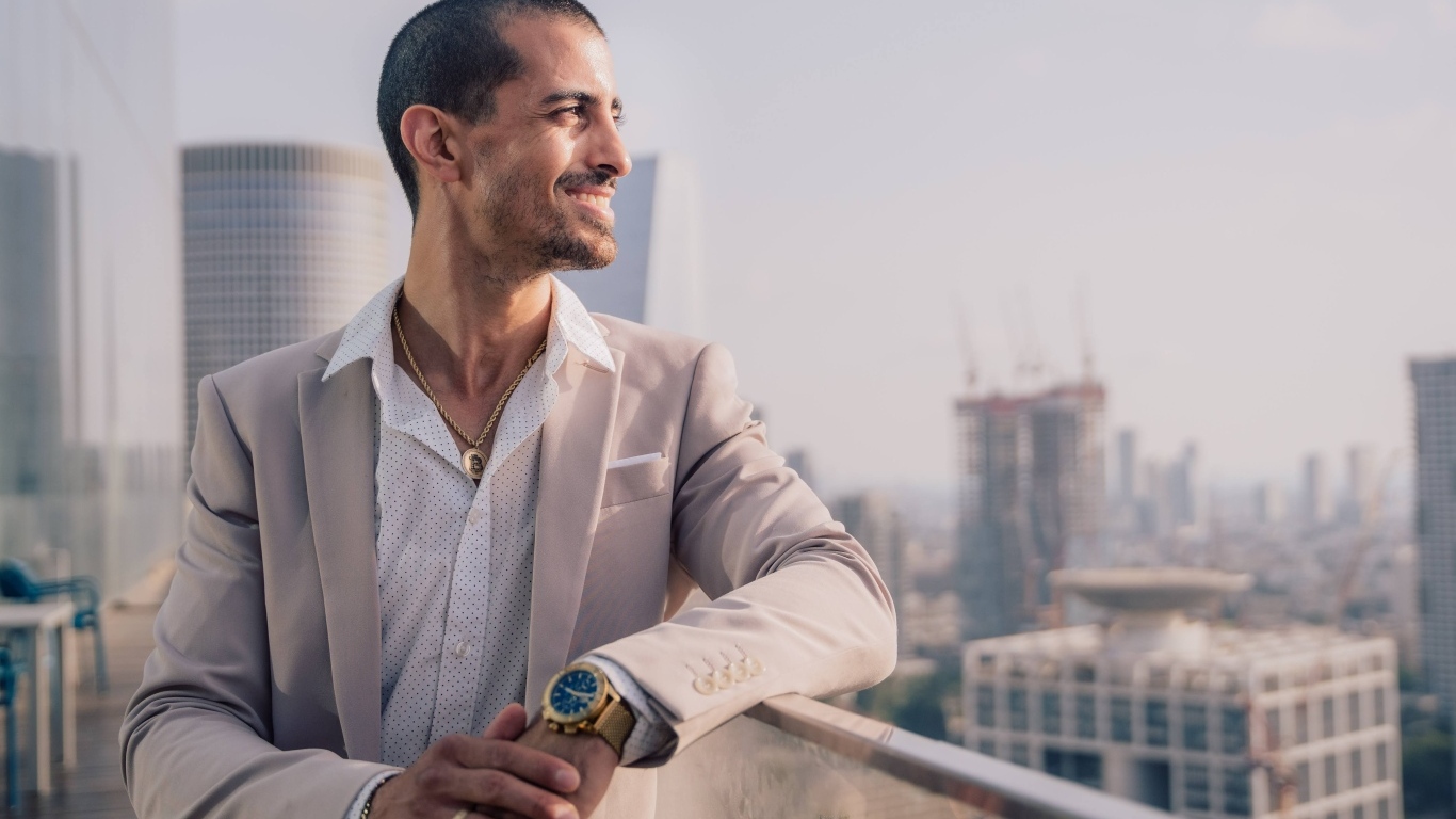 Улыбающийся стильный мужчина в костюме стоит на балконе 