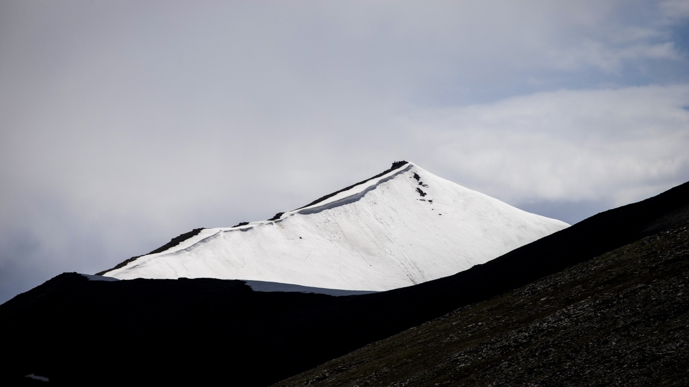 Заснеженная вершина горы под грозовым небом