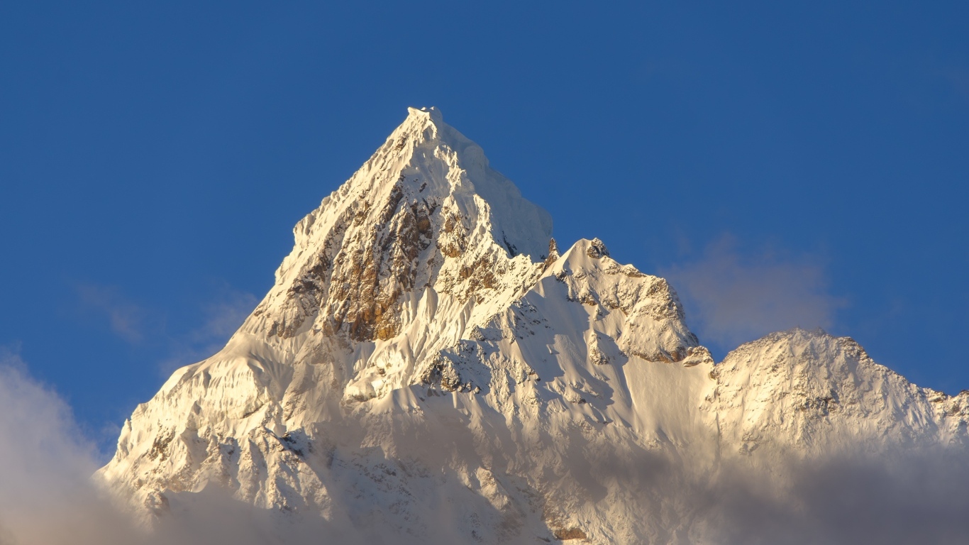 Крутая заснеженная вершина горы на голубом фоне