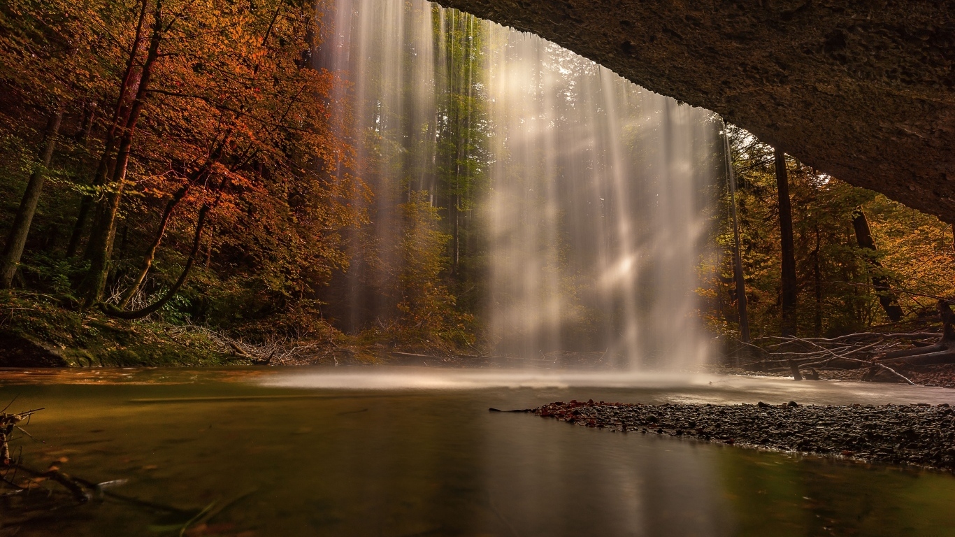 Водопад стекает со скалы в осеннем лесу