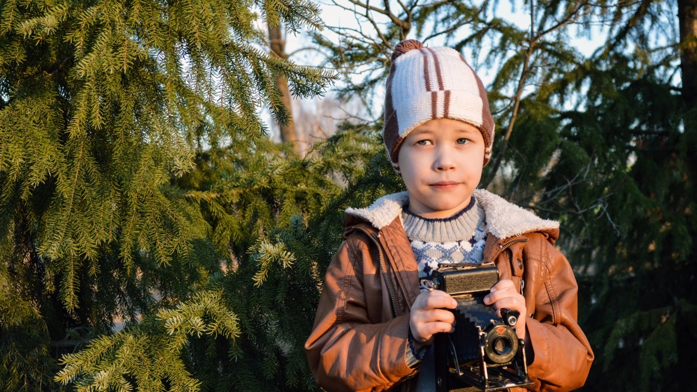 A boy with a camera is standing by the spruce