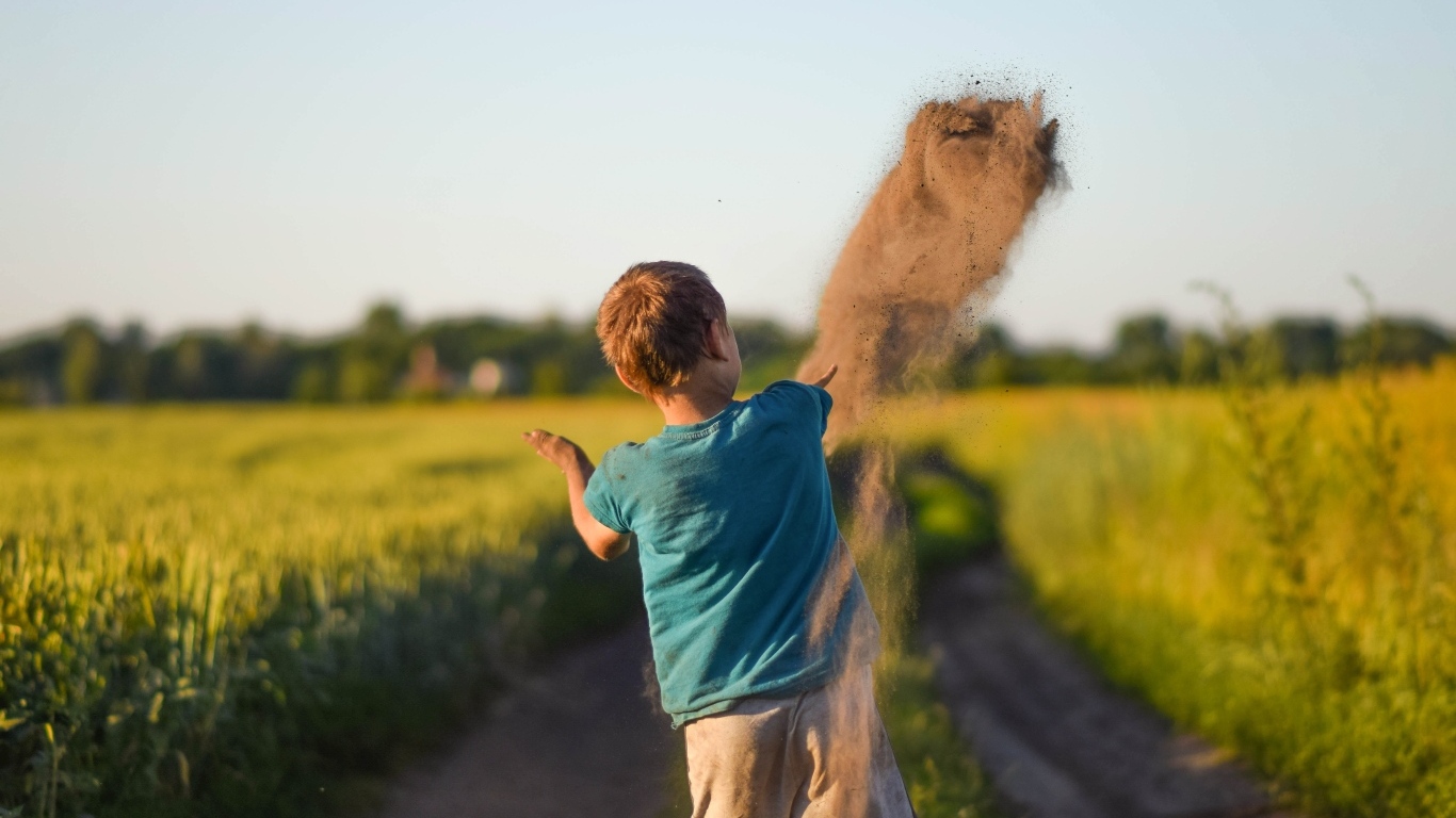 Мальчик бросает песок на дороге