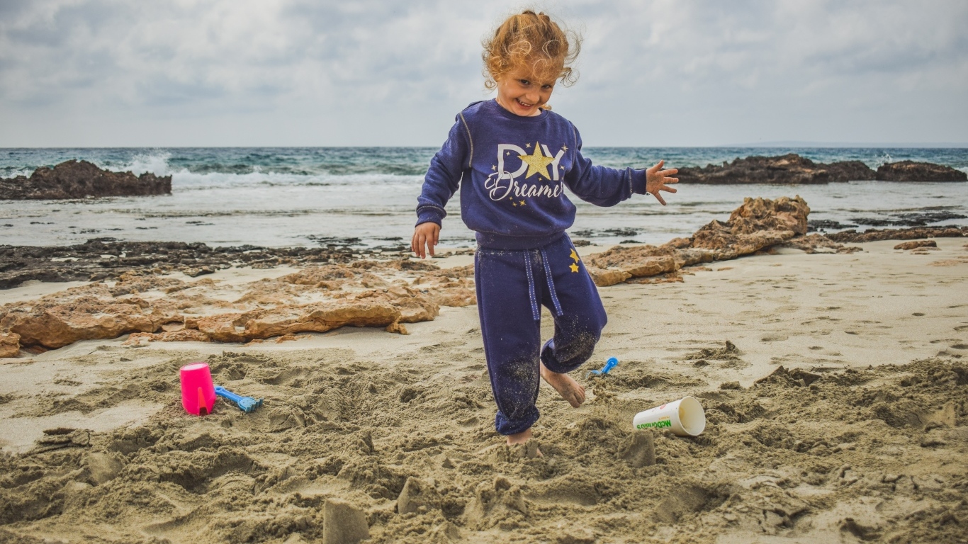 Веселая девочка играет на песке на пляже
