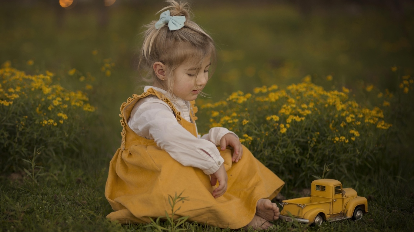 Девочка сидит на траве с игрушечной машинкой