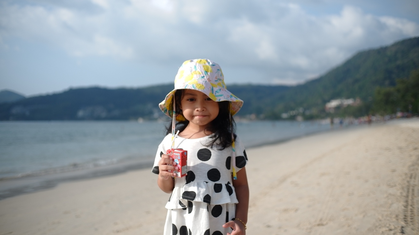 Девочка с соком в руках стоит на пляже