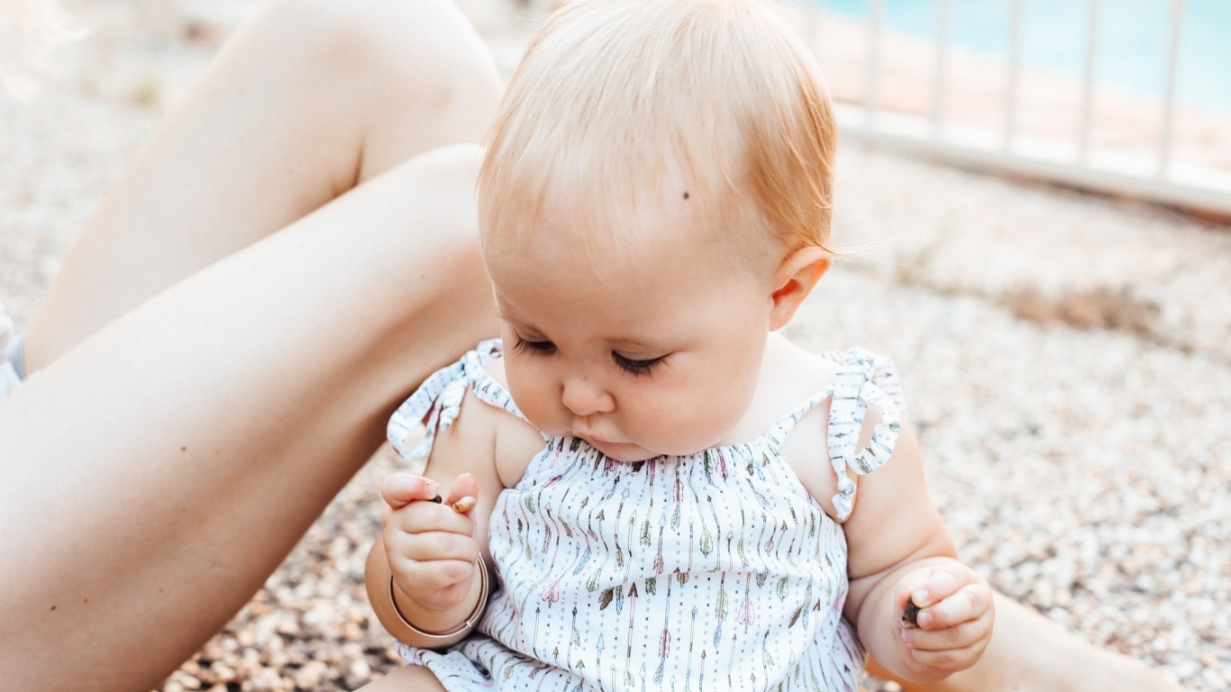 Маленькая светловолосая девочка сидит на песке