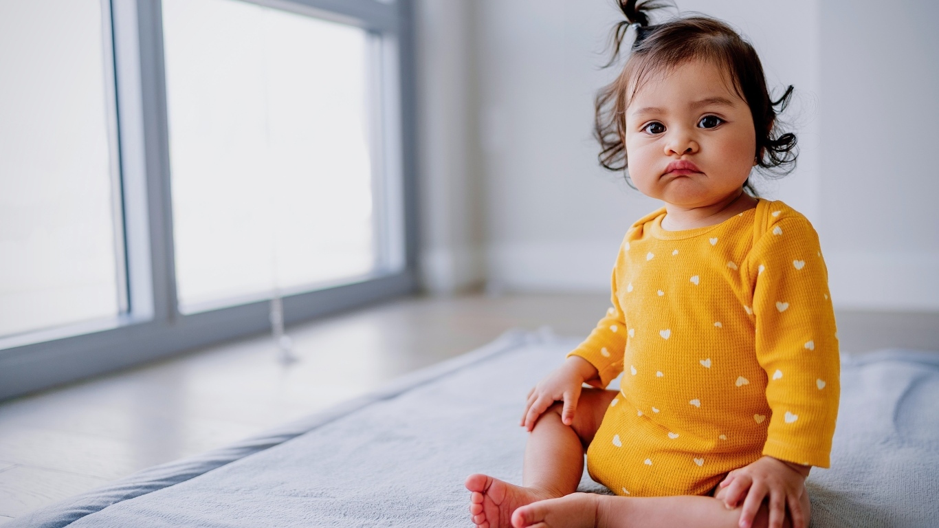 Маленькая смешная девочка сидит у окна