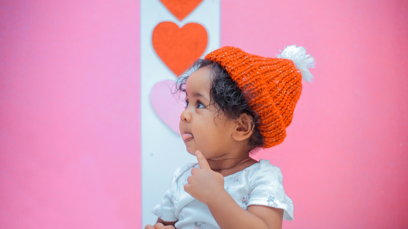 Маленькая девочка в вязаной шапке на розовом фоне