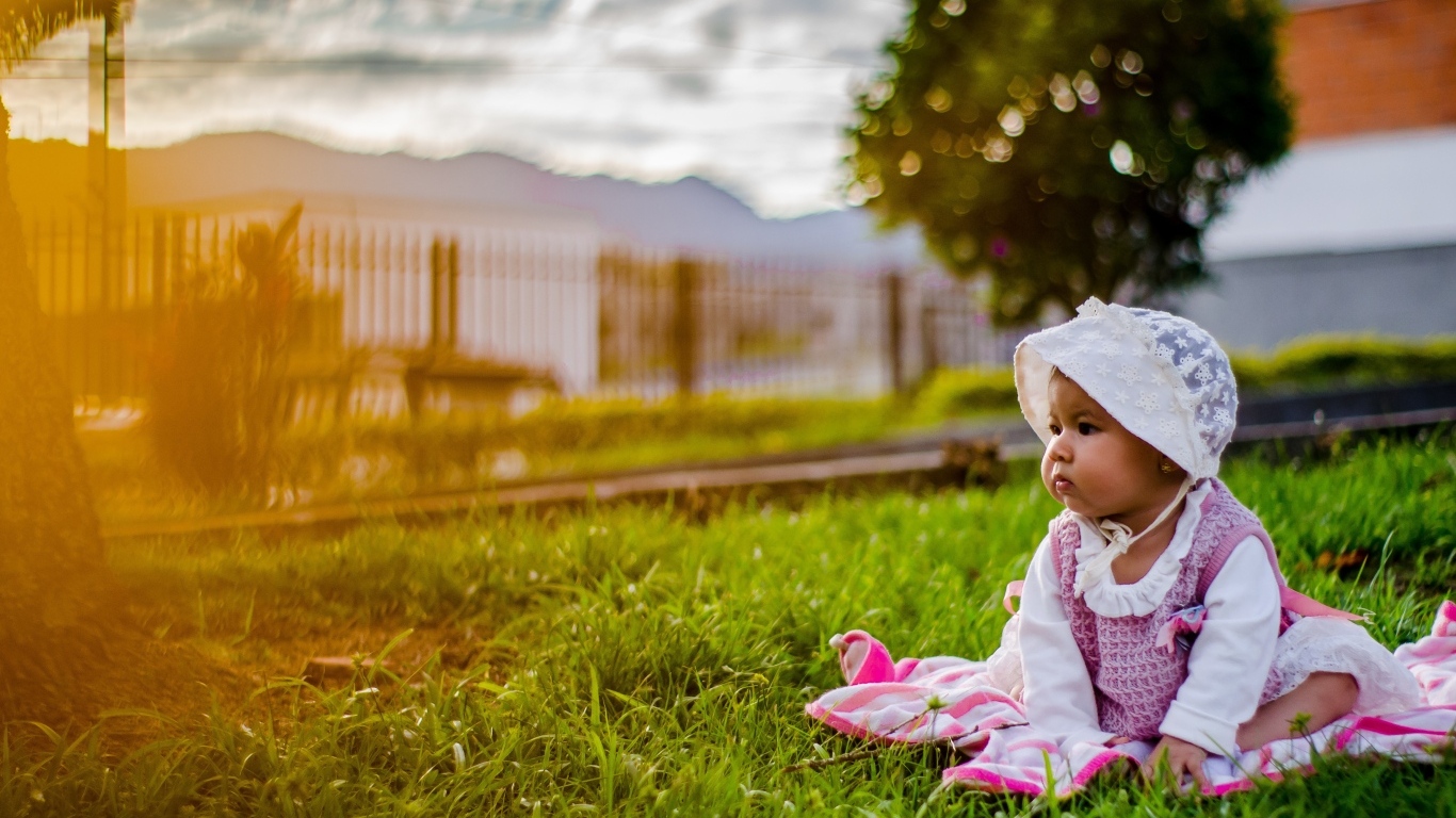 Маленькая девочка в розовом платье сидит на траве