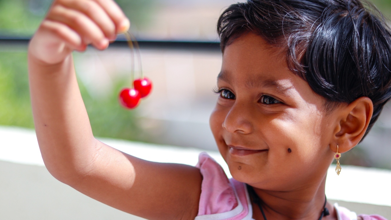 Маленькая улыбающаяся девочка с ягодами вишни в руках