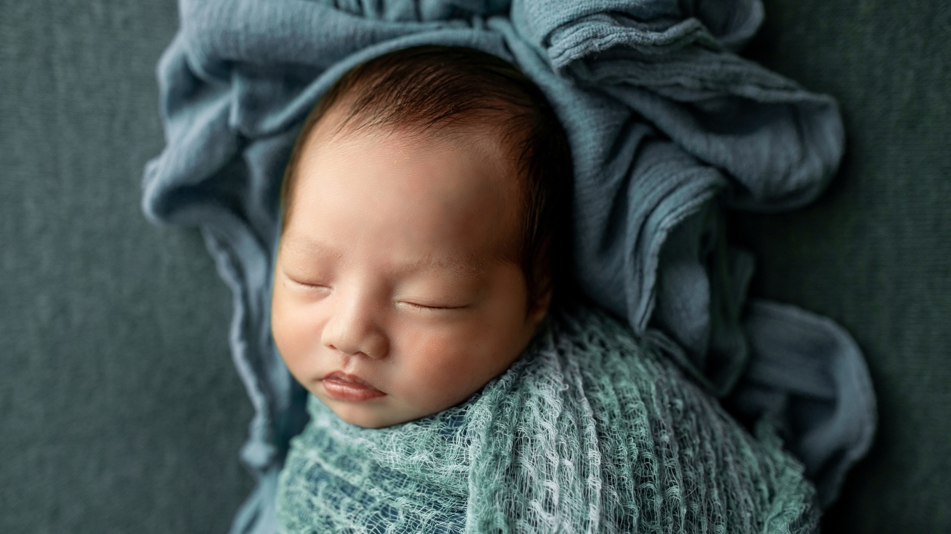 Новорожденный ребенок завернут в серое покрывало 