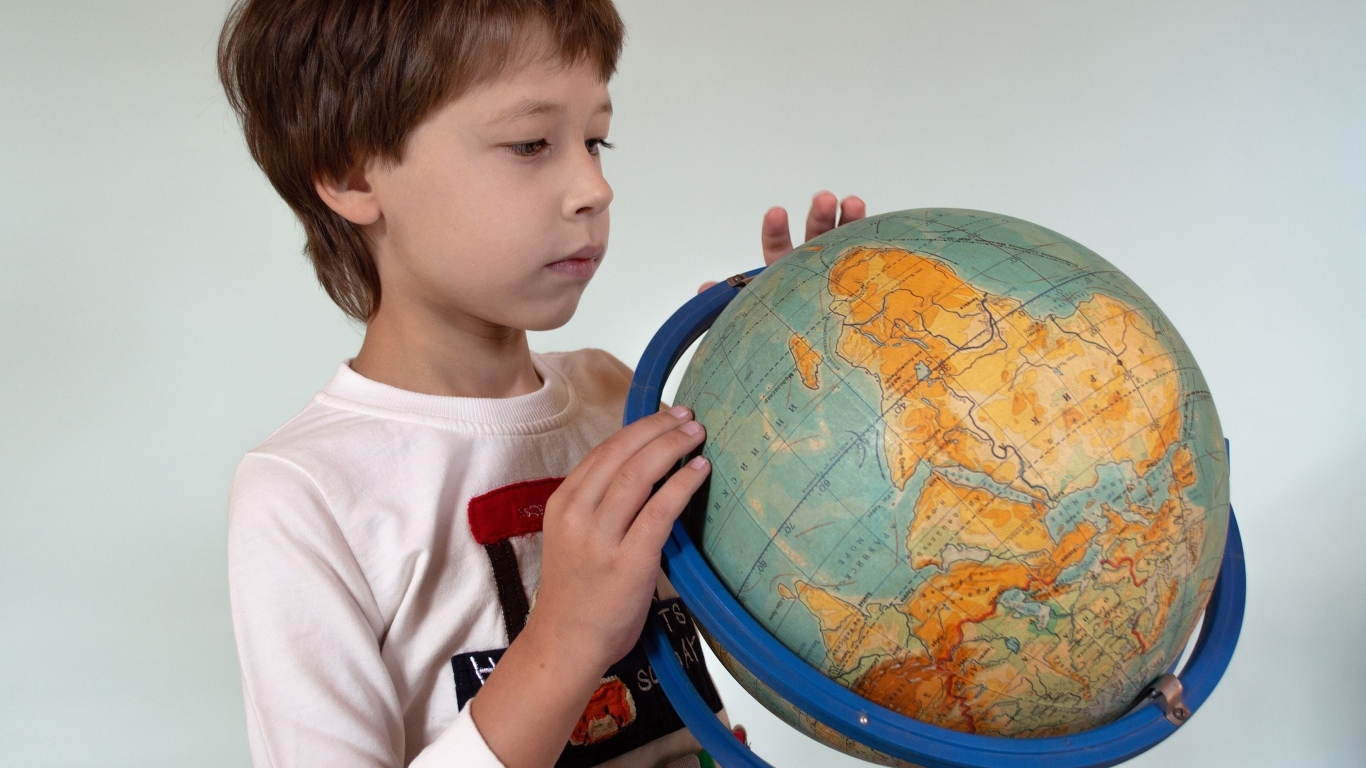 Школьник изучает глобус на сером фоне