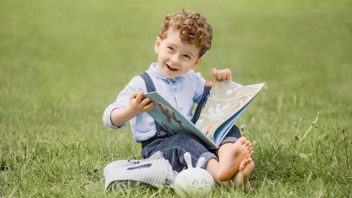 Улыбающийся мальчик с книгой сидит на траве