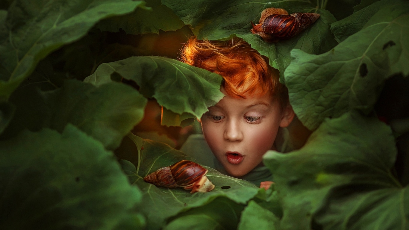 Удивленный рыжеволосый мальчик смотрит на улитку