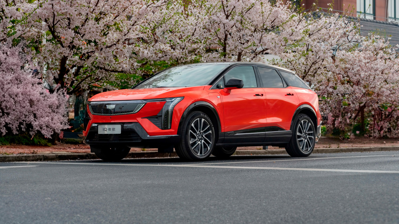 Красный Cadillac Optiq Sport 2024 года у цветущих деревьев