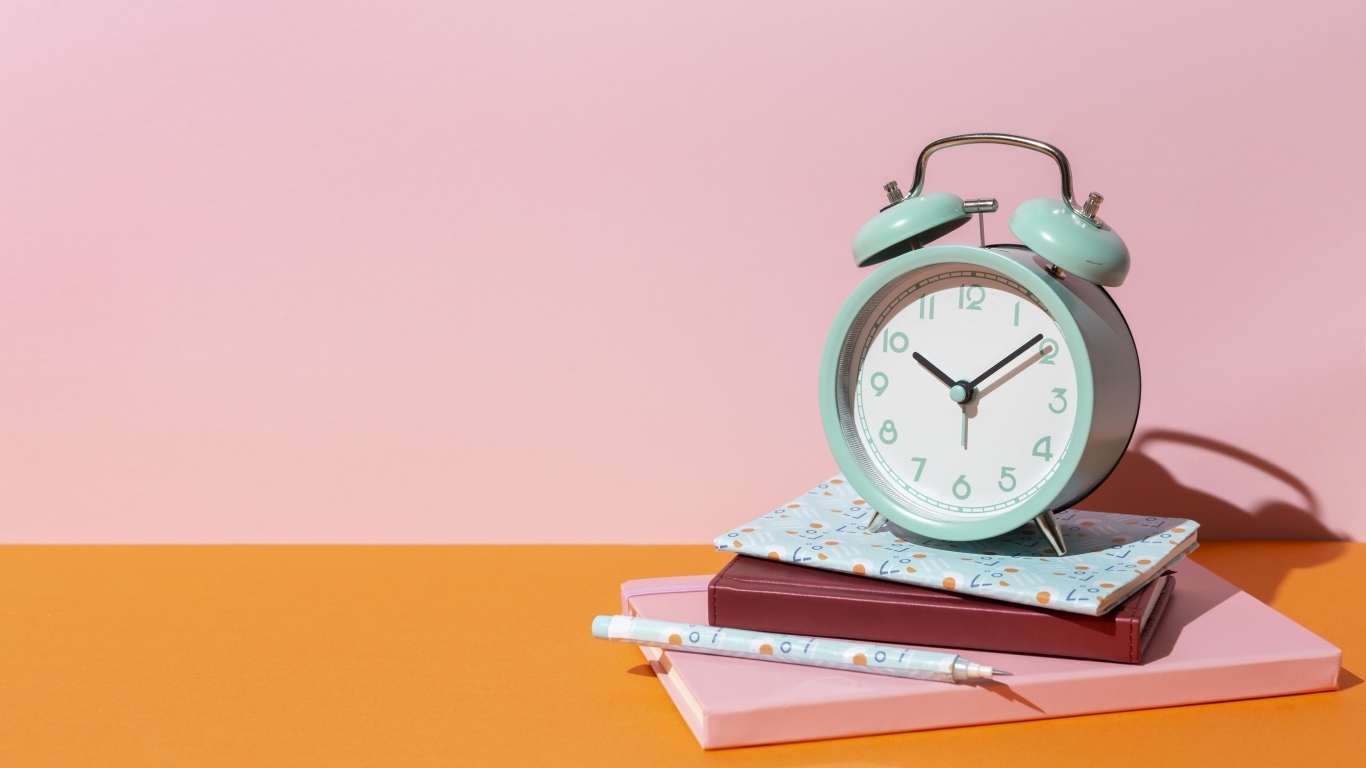 Будильник с книгами на розовом фоне