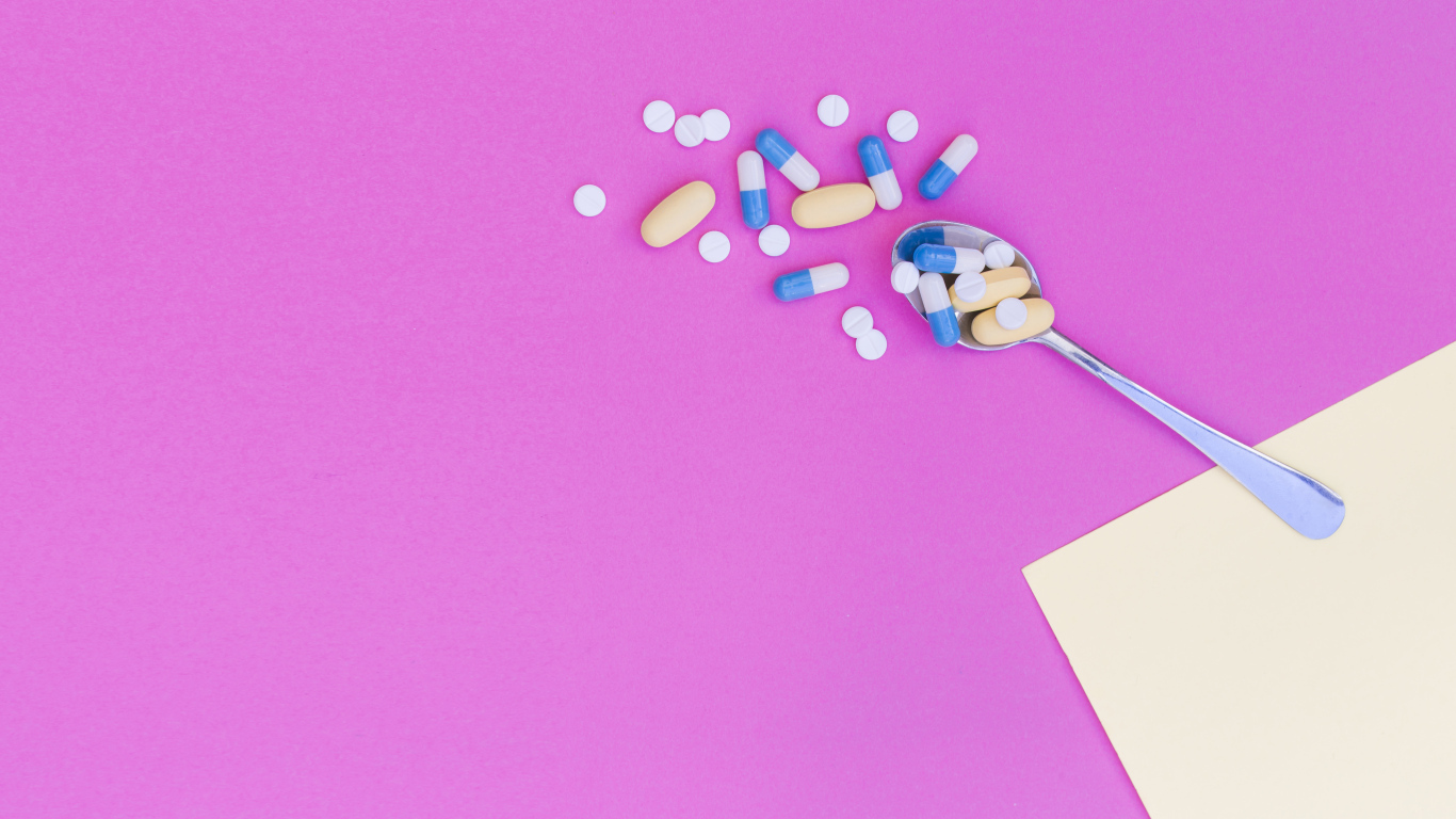 Таблетки с ложкой на розовом фоне