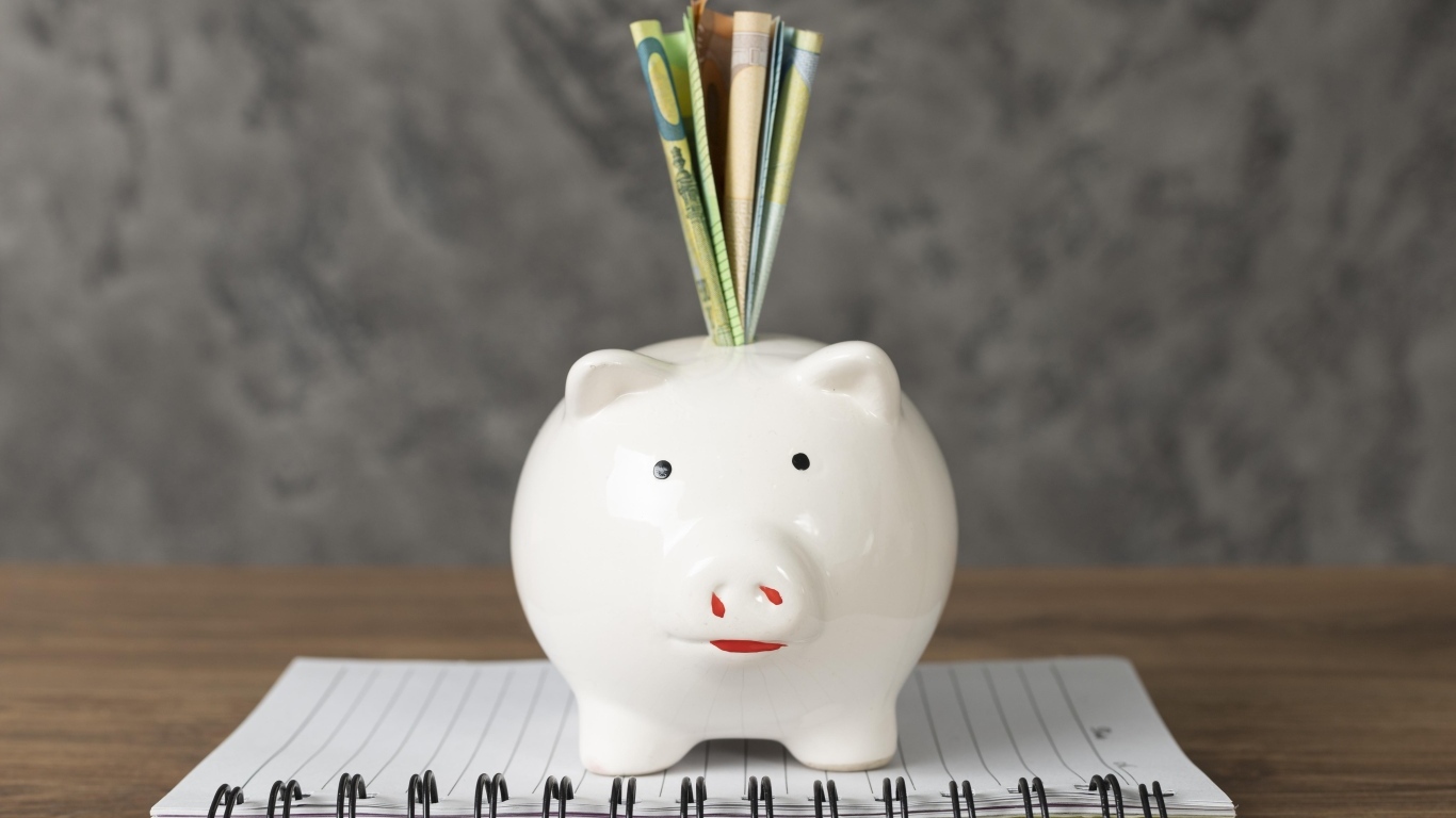 Свинья копилка с купюрами на столе с блокнотом