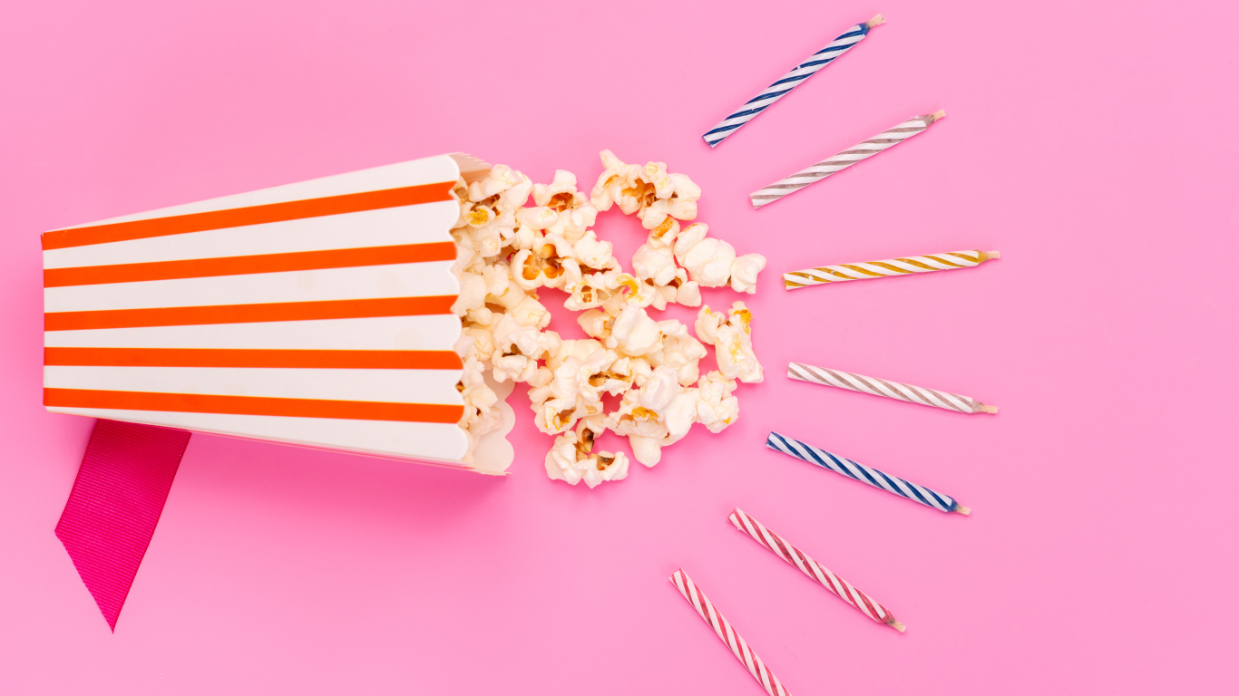 Коробка попкорна со свечами на розовом фоне