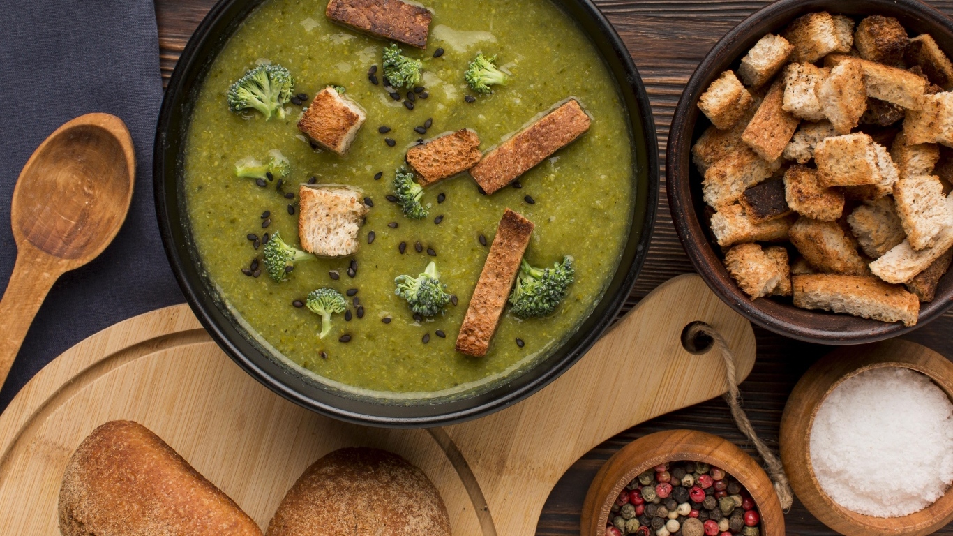 Зеленый суп пюре на столе с сухариками и перцем
