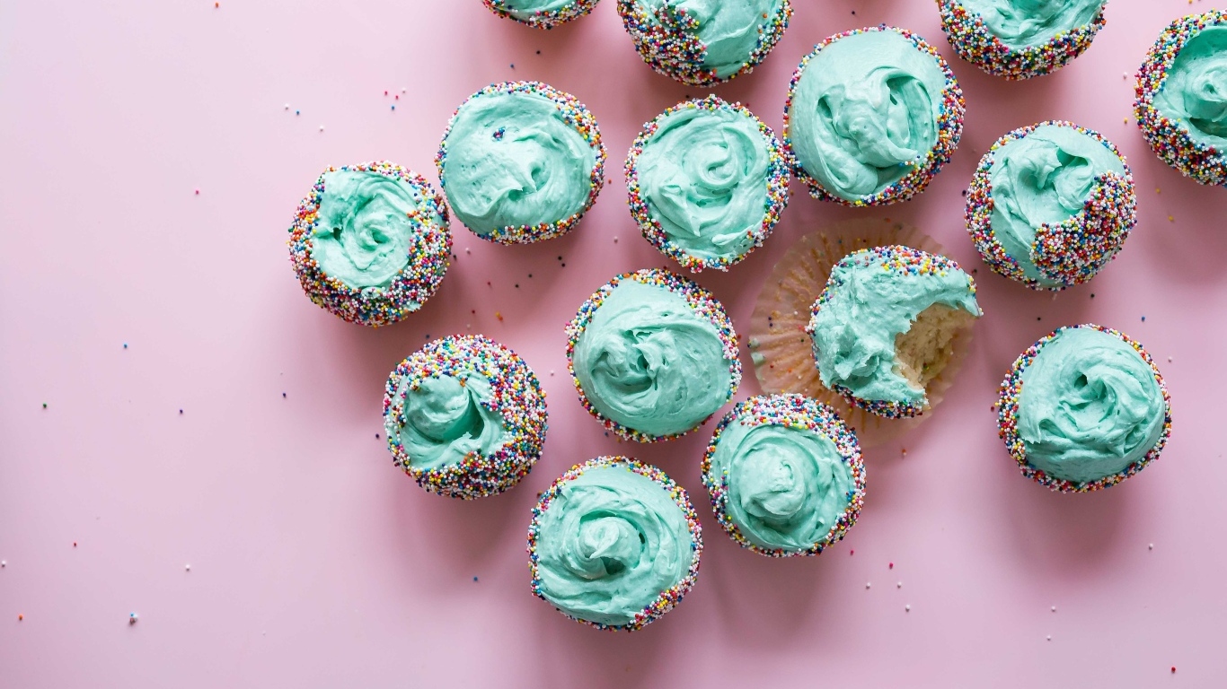 Аппетитные кексы с голубым кремом на розовом столе